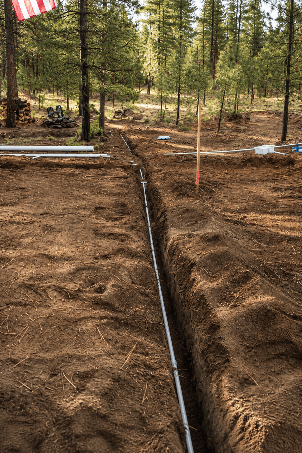 White PVC pipe laid in a long dirt trench at a wooded construction site.